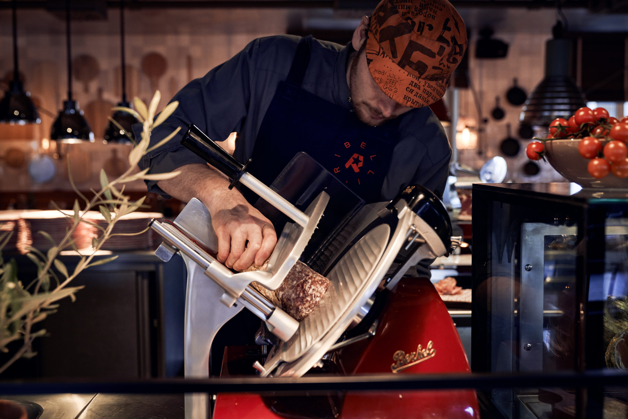 A chef is cutting fresh ham at a slicing machine